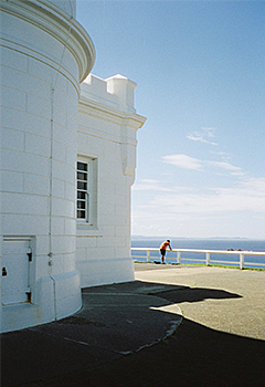 man leaning on railing in front of lighthouse